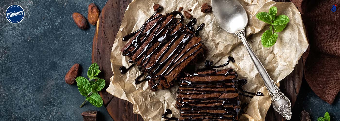 Chocolate cake with drizzled chocolate sauce on top. On a dark wood plate and a silver spoon