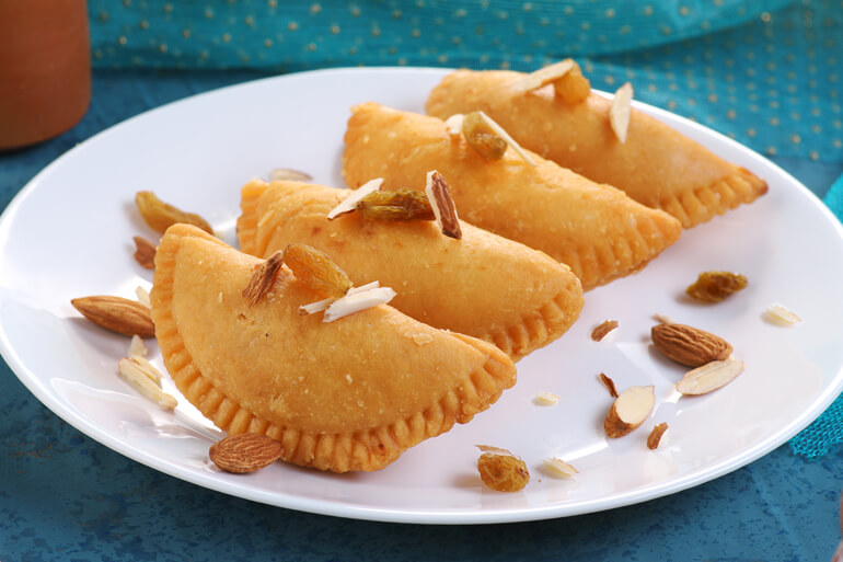 4 Gujiya on a white plate with sliced almonds on top