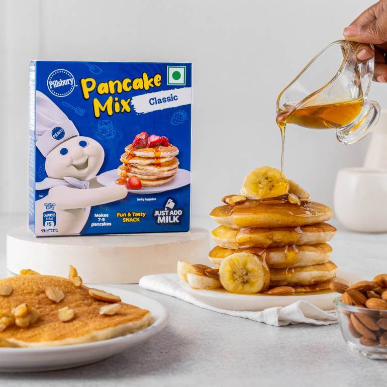 Lifestyle image of a stack of pancakes with bananas and maple syrup with a box of Pancake Mix, Classic flavor in the background