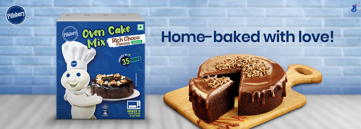 A chocolate cake on a wood cutting board with a box of Pillsbury India Oven Cake Mix Rich Choco flavor in front