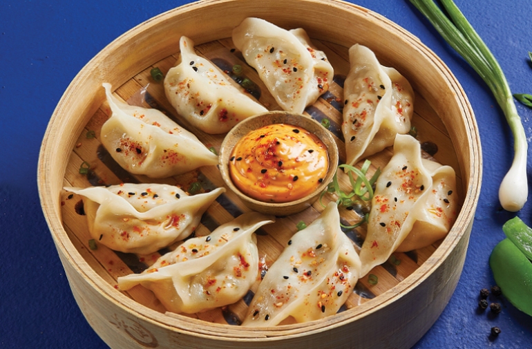 A bowl of Momos with sauce in the middle and red pepper flakes on top